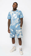 Rear full-body view of a male model showing the back profile of the iLLionaire acid wash blue streetwear shirt and shorts set, highlighting the unique distressed splash pattern across the fabric.