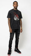 Full-body studio shot of a tattooed male model wearing the iLLionaire Crystal Cupid box cut graphic t-shirt in mineral wash black, styled with black distressed ripped skinny jeans and black Jordan 4 retro sneakers.